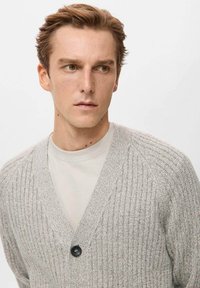 Jasnoszary dziergany sweter z dekoltem w serek i prążkowaną fakturą. Posiada pojedynczy czarny guzik oraz prosty, warstwowy fason noszony na koszulce.