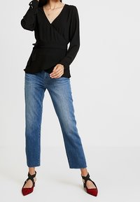 Sort slå-om-bluse med lange ærmer, kombineret med lyseblå jeans med lige ben. Skoene er røde med leopardprint og sorte remme.