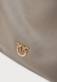 Bolso de mano de cuero marrón con un herraje circular de tono dorado y dos motivos de aves. Textura suave y diseño minimalista.