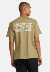 Beige cotton t-shirt featuring a white graphic design on the back, depicting palm trees and waves, with a relaxed fit and short sleeves.