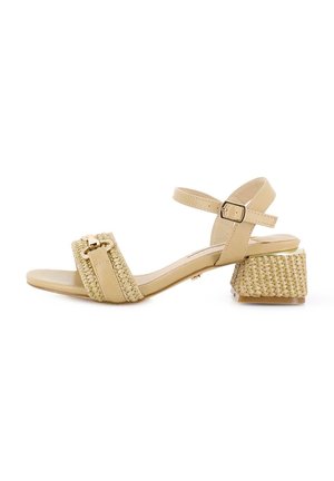 Sandalia de tacón beige con detalle de tira trenzada, hebilla en el tobillo y un tacón cuadrado texturizado. Parte superior de cuero suave y puntera redondeada.