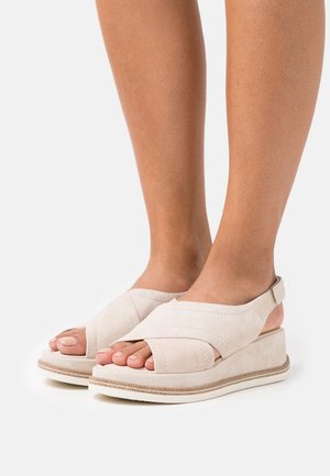 Beige suède wedge sandalen met open teen en kruisbandontwerp, voorzien van een getextureerde zool en een kleine hielband voor extra ondersteuning.