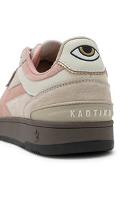 Sneaker mit einem Obermaterial aus beigem Wildleder und Leder, rosa Akzenten, einer braunen Gummisohle und einer markanten Augen-Grafik an der Ferse.