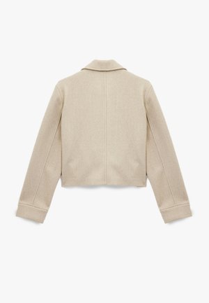 Chaqueta corta beige de tela suave con cuello de muesca, con mangas largas y costuras visibles en la parte posterior. Textura lisa sin patrones.