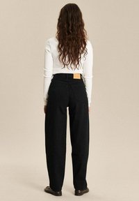 Zwarte wijde denim broek met een hoge taille en achterzakken. Kenmerkend zijn het tankleurige merklabel op de tailleband en de soepele textuur.