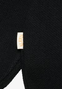 Schwarzer gestrickter Schal mit einem strukturierten Muster, versehen mit einem weißen Etikett, auf dem der Markenname in goldenen Buchstaben eingestickt ist.