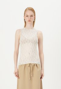 Krajkový top na ramínka v bílé barvě s jemným květinovým vzorem. Má kulatý výstřih a bezrukávový design, doplněný o béžovou sukni na stažení.