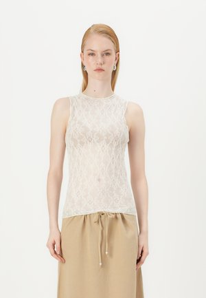Débardeur en dentelle blanche avec un délicat motif floral. Il présente un col rond et un design sans manches, associé à une jupe beige à cordon de serrage.