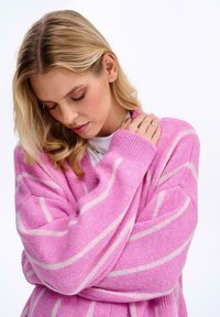 Růžový pletený cardigan s bílými pruhy, design do V, dlouhé rukávy, texturovaná tkanina a oversized střih. Bez viditelných zapínání a kapes.