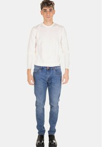 Camicia bianca a maniche lunghe, jeans di denim blu e scarpe nere. Jeans a taglio dritto con dettagli di cuciture, camicia liscia senza motivi.