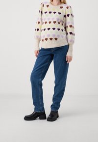 Pull en maille avec des motifs de cœurs multicolores dans des tons de violet, marron et jaune. Poignets ajustés et coupe décontractée associés à un jean en denim ample.
