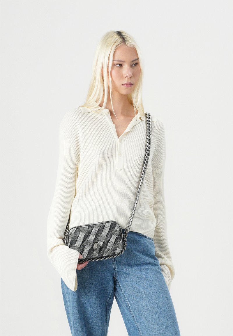 Hellbeige, gerippter Strickpullover mit Kragen und oversized Ärmeln, kombiniert mit Jeans und einer schwarz-weißen gemusterten Umhängetasche mit Kettenriemen.