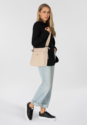 Borsa a spalla beige realizzata in materiale morbido e liscio. Presenta una forma rettangolare semplice, tracolla regolabile e dettaglio del logo sul davanti.