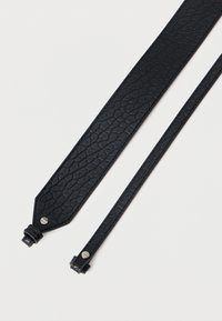 Melnā teksturētā ādas siksna ar rāpuļa ādas rakstu, ar metalizētiem akcentiem abos galos un elegantā, iegarena formā.