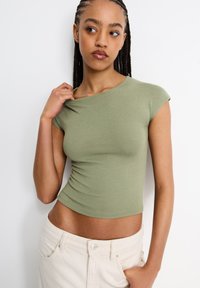 Ljusgrön, figurnära, kortärmad cropped top av mjukt tyg med rund halsringning. Kombineras med ljusa byxor som visar en strömlinjeformad siluett.