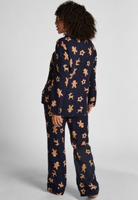 Marineblauw pyjamaset met een overal print van peperkoeken mannen, rendieren en sterren. De stof heeft een zachte textuur met uitlopende broekspijpen.