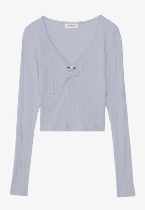 Haut court à manches longues bleu clair avec texture côtelée, décolleté en V, détail froncé à l'avant et une épingle décorative au centre.