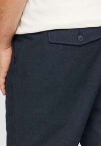 Pantalons bleu foncé en tissu texturé, dotés d'une poche avant avec fermeture à bouton et de détails de couture sur les côtés.