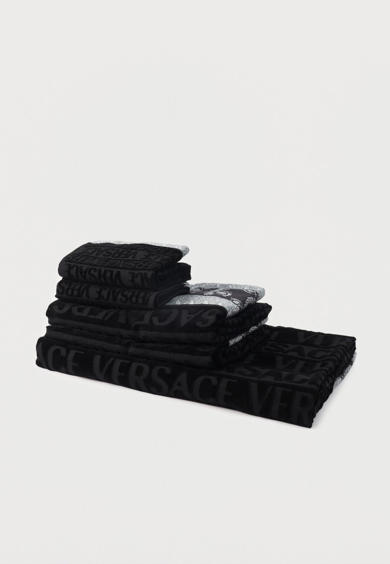 Στοίβα από μαύρες και γκρι πετσέτες με το ανάγλυφο λογότυπο "Versace", τοποθετημένες σε φθίνουσα σειρά μεγέθους πάνω σε λευκό φόντο.