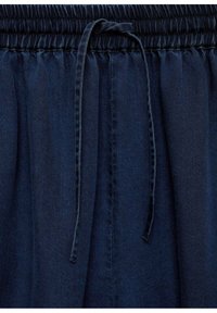 Pantalones con cinturilla elástica y cordón en color azul marino. Presentan una textura lisa de mezclilla y detalles plisados para un ajuste relajado.