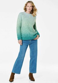 Flauschiger, verlaufender Pullover in Grün- und Blautönen, Rundhalsausschnitt, kombiniert mit hellblauen Jeans und braunen Absatzstiefeln.