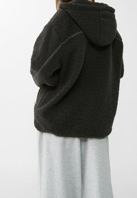 Donkergrijze fleece jas met capuchon, met een gestructureerde buitenkant, een losse pasvorm en subtiele stiksels langs de schouders.