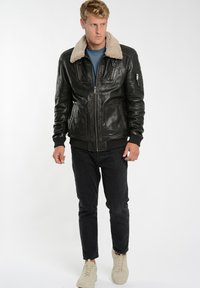Svart läderjacka med fårskinnskrage, dragkedja fram, två framfickor, ribbade ärmslut och nederkant; bärs med mörka jeans och beige sneakers.