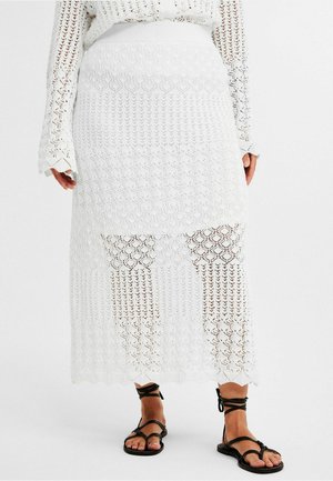 Witte gehaakte maxi rok met een patroonontwerp, een aansluitende taille en een scalloped zoom. Gecombineerd met platte zwarte sandaaltjes met banden.