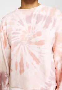 Felpa in cotone di un delicato rosa, con un motivo a spirale tie-dye impreziosito da accenti pesca e lavanda. Collo a giro e polsini a coste.