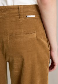Bruine corduroy broek met een zachte textuur, voorzien van een achterzak en een label op de tailleband met de tekst "Marc O'Polo Denim."