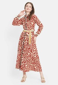 Abito lungo con motivo a fiori in rosso e crema. Presenta una zip frontale, una vita con cintura e maniche arricciate con dettagli in pizzo.