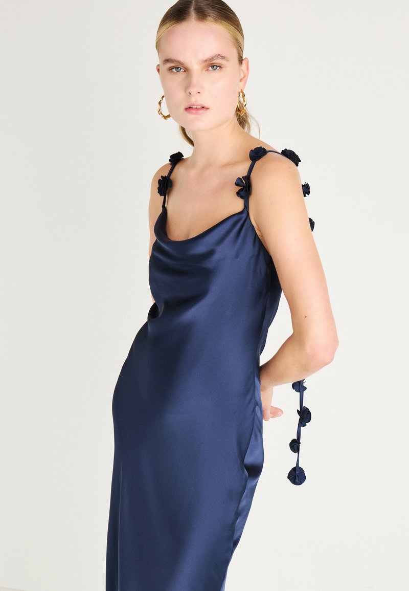 Rochie din satin de culoare bleumarin, cu o croială lejeră, având accente florale pe bretele și o textură fină. Design elegant și minimalist, cu o siluetă fluidă.