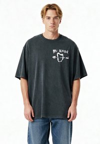 T-shirt noir en coton surdimensionné avec une finition délavée, présentant un texte graphique blanc "Mi Amor" et un design de cœur avec des flèches sur le devant.