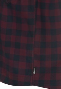Chemise à carreaux rouge et marine avec une texture lisse, dotée d'un ourlet et d'une étiquette de marque sur la coutures latérale.
