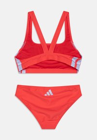 Crveni atletski bikini set s sportskim grudnjakom s prekrivenim trakama i odgovarajućim bikinijem. Sadrži svijetloplave akcentne detalje.