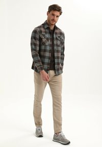 Geruite flanellen overhemd in bruin, grijs en teal met twee borstzakken, gecombineerd met beige broeken en grijze sneakers. Gelaagd stof, met knoopsluiting.