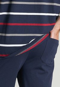 Gestreiftes Kurzarmhemd in Marineblau, Weiß, Grau und Rot. Mit einer Tasche mit Reißverschluss an der marineblauen Hose. Der Stoff ist eine glatte Baumwollmischung.