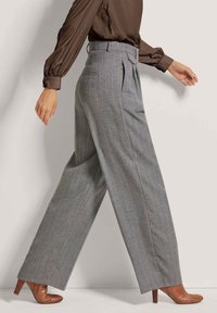 Grijs gestreepte broek met een hoge taille en wijde pijpen, voorzien van oranje lijnen, en gecombineerd met bruine hakken.