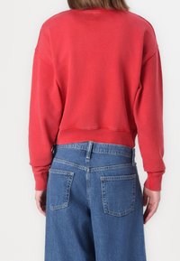 Sudadera roja recortada con puños y cuello acanalados, combinada con unos vaqueros de denim azul claro de cintura alta con bolsillos traseros.