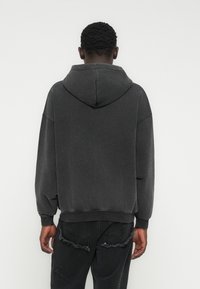 Dunkelgrauer Kapuzenpullover mit lockerem Schnitt, ausgestattet mit einem gerippten Saum, überschnittenen Schultern und weicher Stofftextur. Kombiniert mit schwarzen, distressed Jeans.