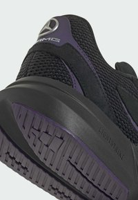 Black athletic shoe featuring mesh material, purple accents, textured rubber sole with a patterned tread, and a logo on the heel.