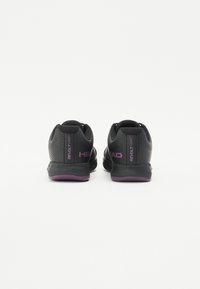 Black athletic shoes with purple accents, textured mesh upper, smooth sole, and visible branding. Designed for court sports.