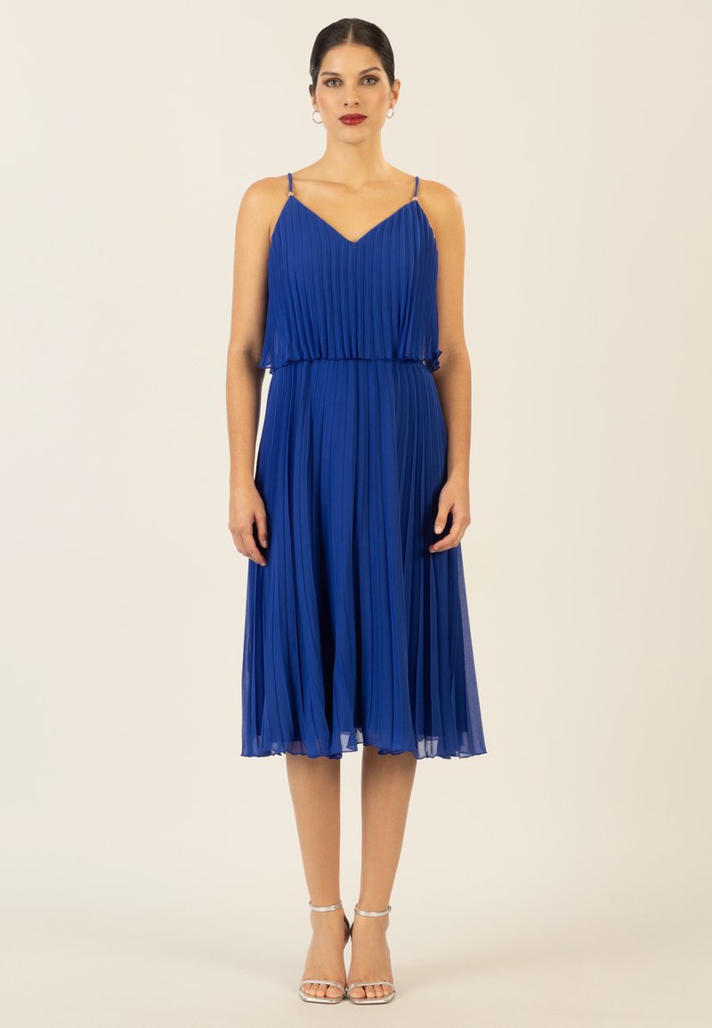 Faltenblaues Kleid mit dünnen Trägern, V-Ausschnitt und einem fließenden Rock. Gestylt mit silbernen Riemchenabsätzen. Glattes, leichtes Material.