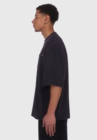 Sort oversized t-shirt lavet af bomuld, med korte ærmer, rund halsudskæring og en brystlomme med en metalaccent.