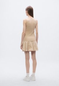 Top beige sin mangas de punto con textura acanalada combinado con una falda beige plisada, usado con zapatillas blancas y calcetines tobilleros con estampado.