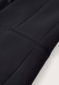 Czarna tkanina o gładkiej fakturze, z przeszytym szwem i subtelnym detalem kieszeni, prezentująca elegancki, minimalistyczny design.