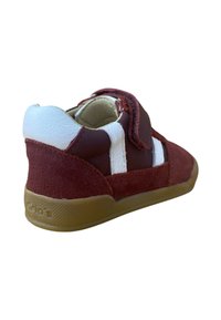 Zapato para niño pequeño en rojo y blanco con tira de velcro, materiales de ante y cuero, y suela de goma, mostrado desde un ángulo lateral trasero.