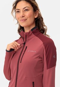 Giacca in pile di un profondo colore rosa con tessuto testurizzato. Presenta un alto colletto, tasche con zip e maniche scure a contrasto.