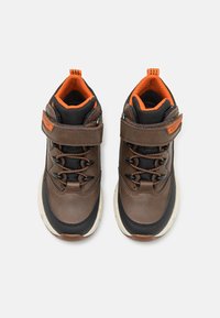 Chaussures de randonnée brunes avec accents noirs, tige texturée, doublure orange et sangle ajustable. Comprend des lacets et une semelle rembourrée.