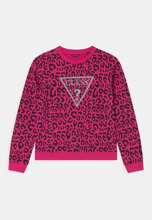 Jasnoróżowa bluza z długim rękawem z czarnym nadrukiem w panterkę oraz srebrnym, brokatowym logo Guess w kształcie trójkąta na środku klatki piersiowej.